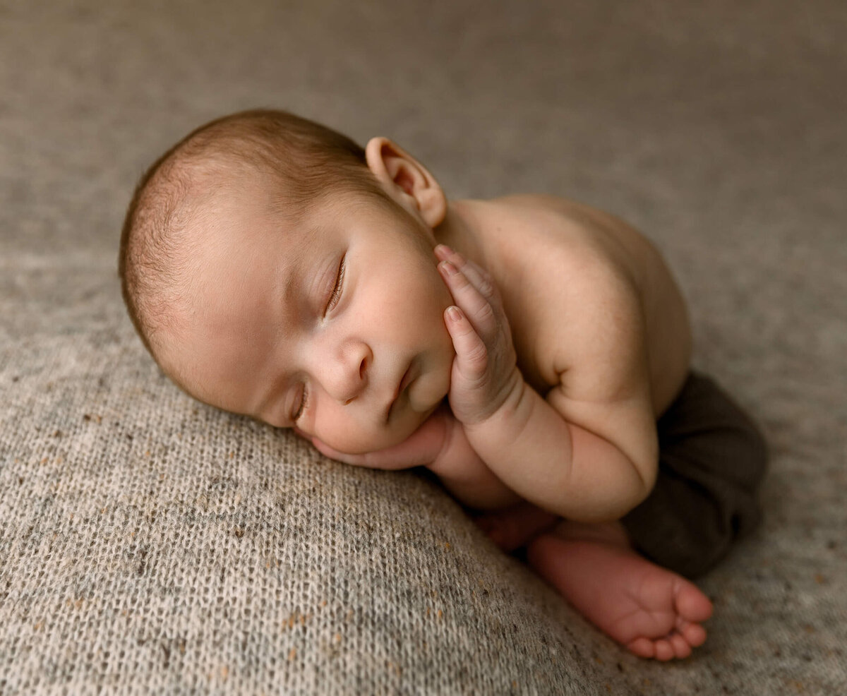 Infant baby boy in a fallen froggie pose laying on a brown backdrop in a photography studio