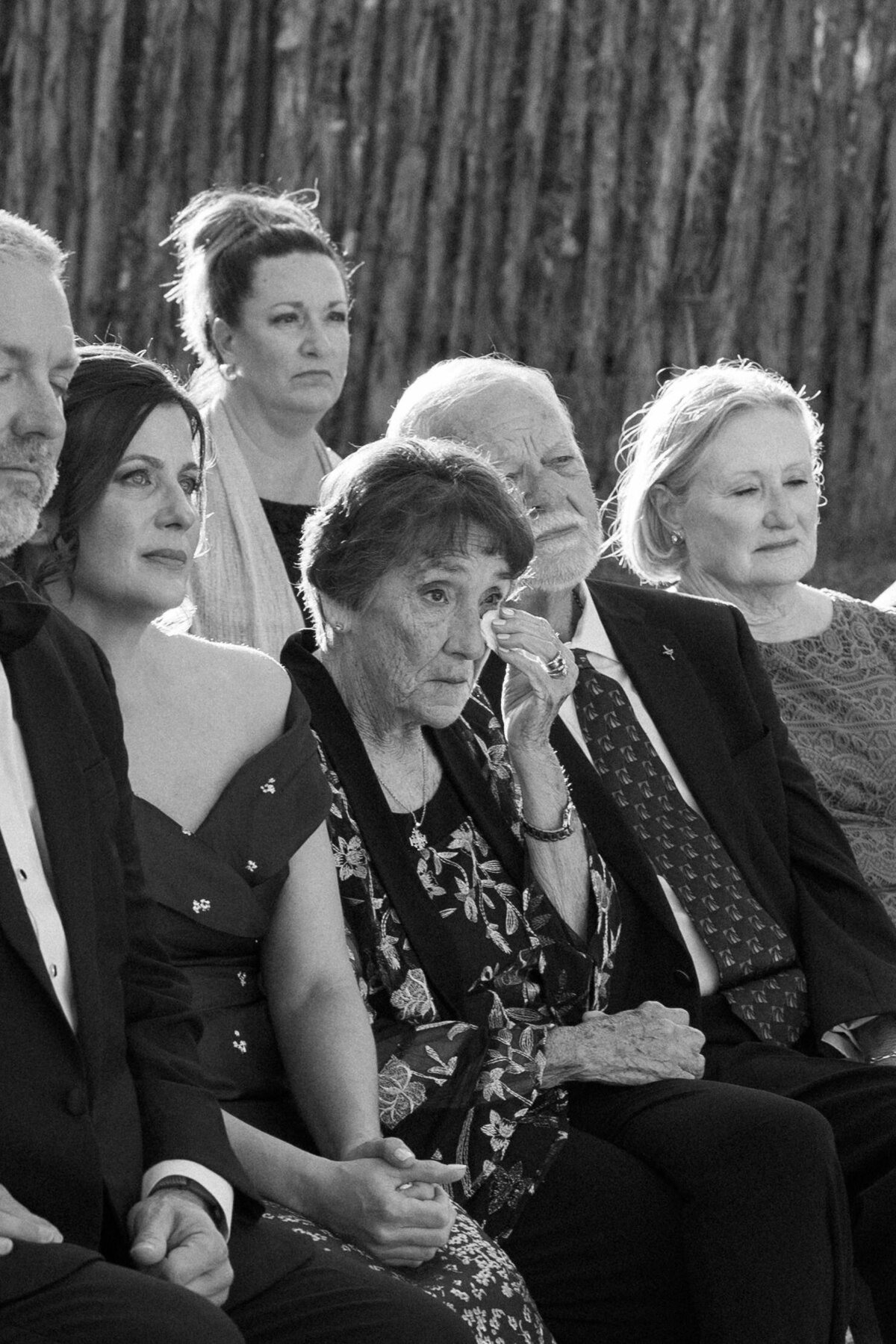 A grand mother wiping a tear from her eye at a ceremony. 