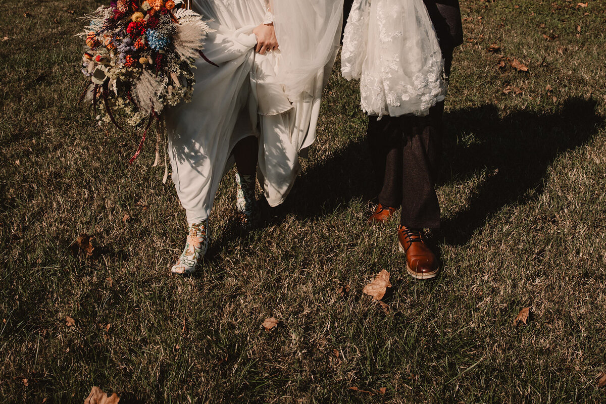 A person holding up the bottom of their wedding dress as they walk in the grass