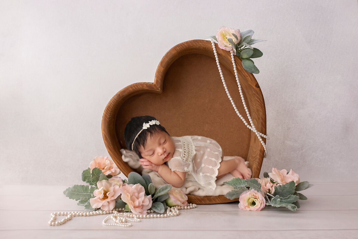 beautiful baby girl posed in a wooden heart prop with roses and pearls arounfd