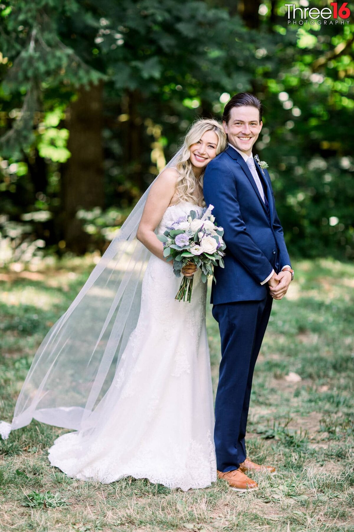 Bride snuggles up to her Groom from behind as they smile for the wedding photographer