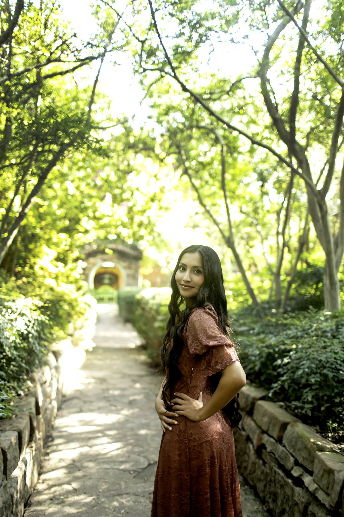 A high school senior radiating joy as she poses near the colorful flowers and stone pathways at Chandor Gardens in Weatherford, TX