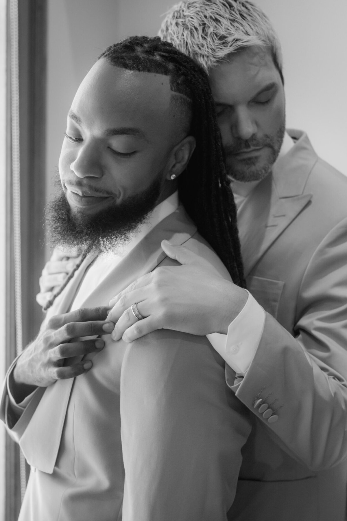 Two men in suits standing in a warm embrace with eyes closed.