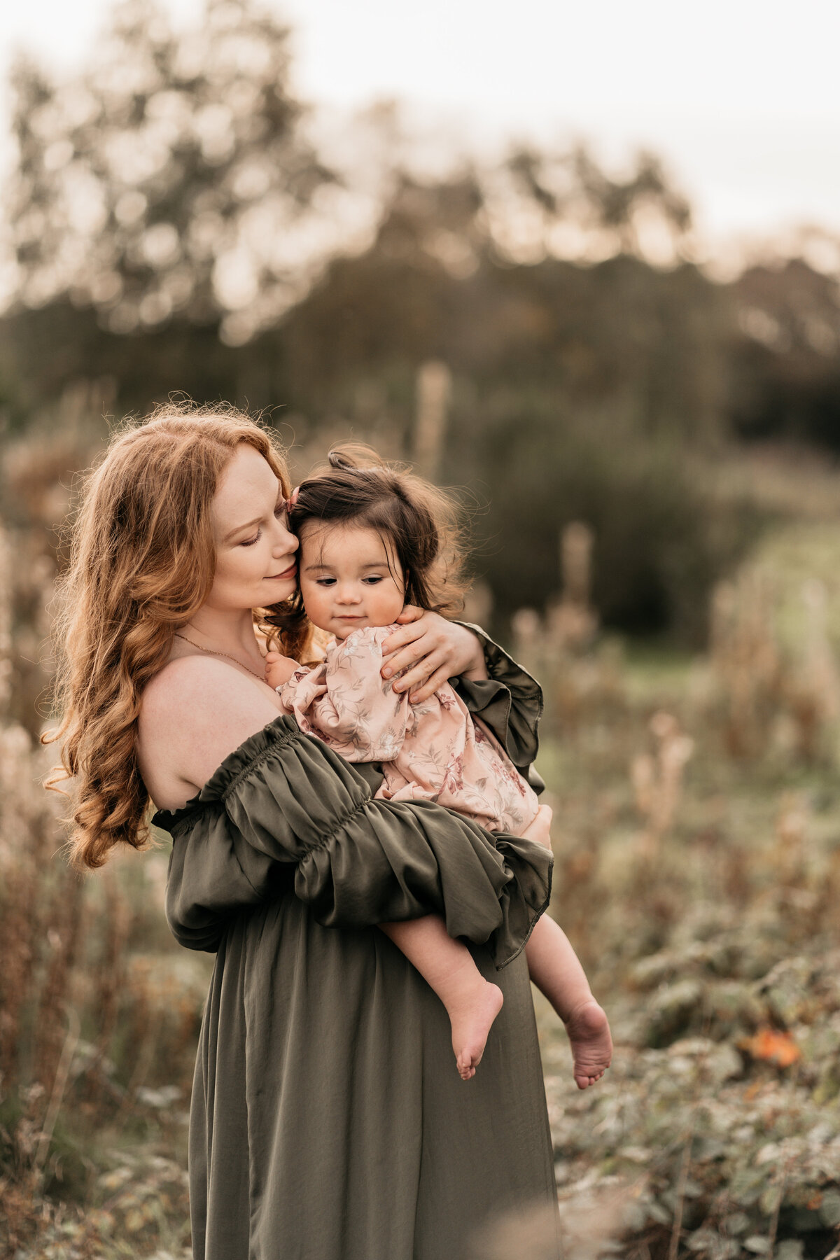 Photo of a pregnant woman in a green dress holding her daughter
