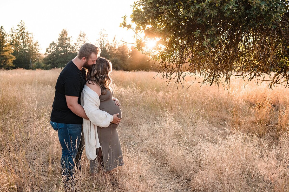 couple maternity photos with husband kissing wife at sunset in field.