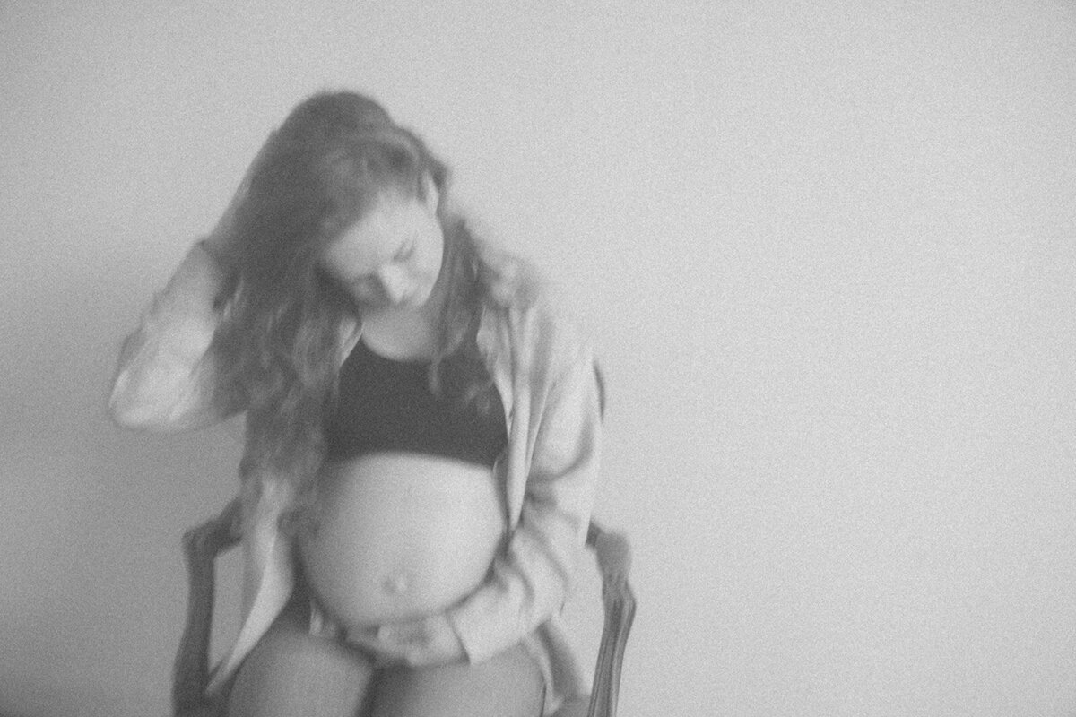 Woman plays with her hair while resting her hand on her pregnant belly during a photo session. 