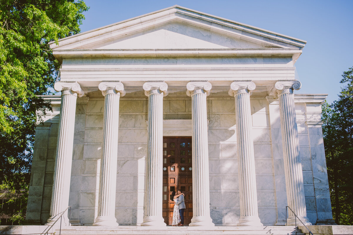 An engaged couple stand in the middle of a white column building at princeton university