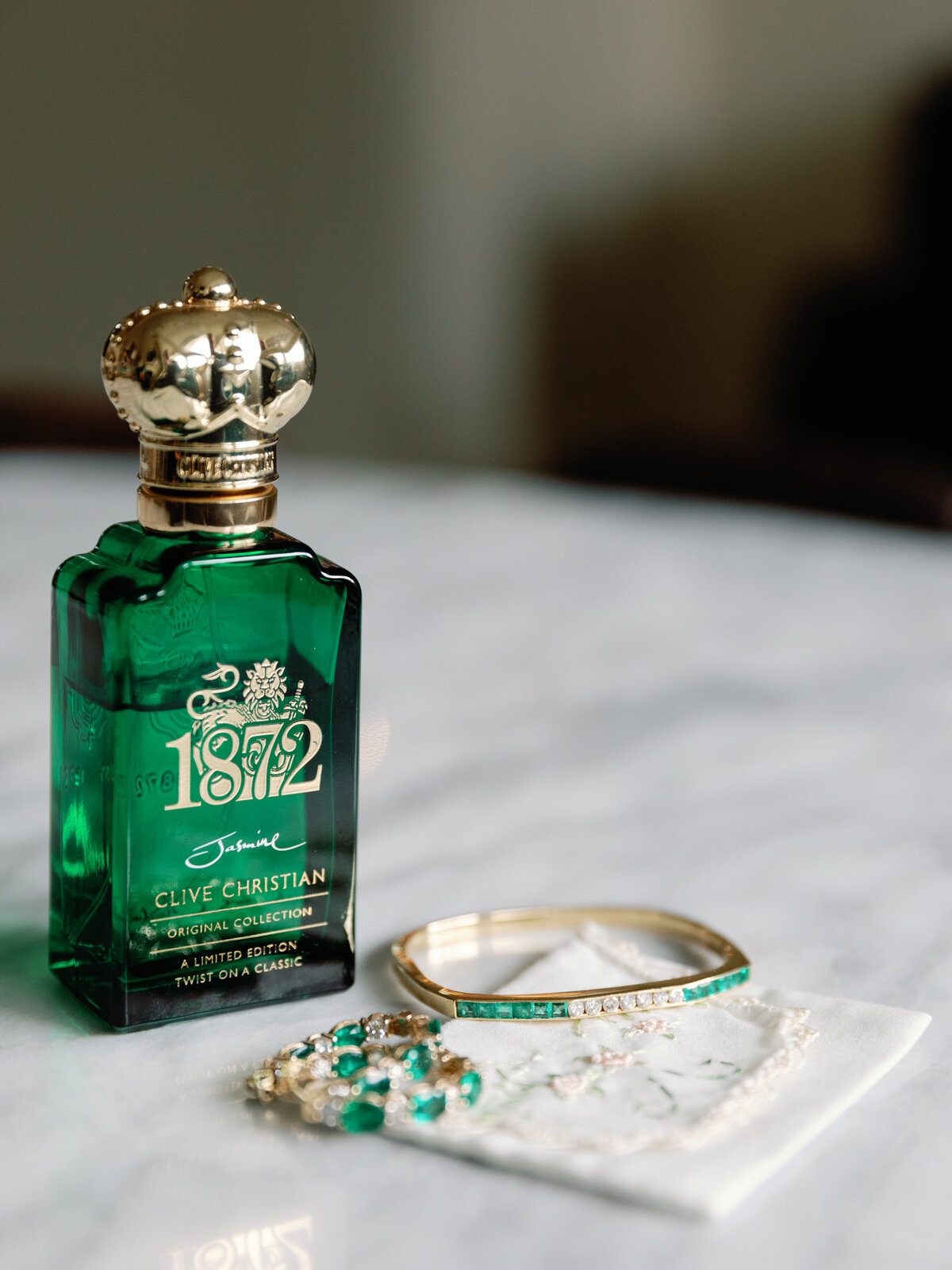 green and gold perfume bottle and jewelry laying on white marble