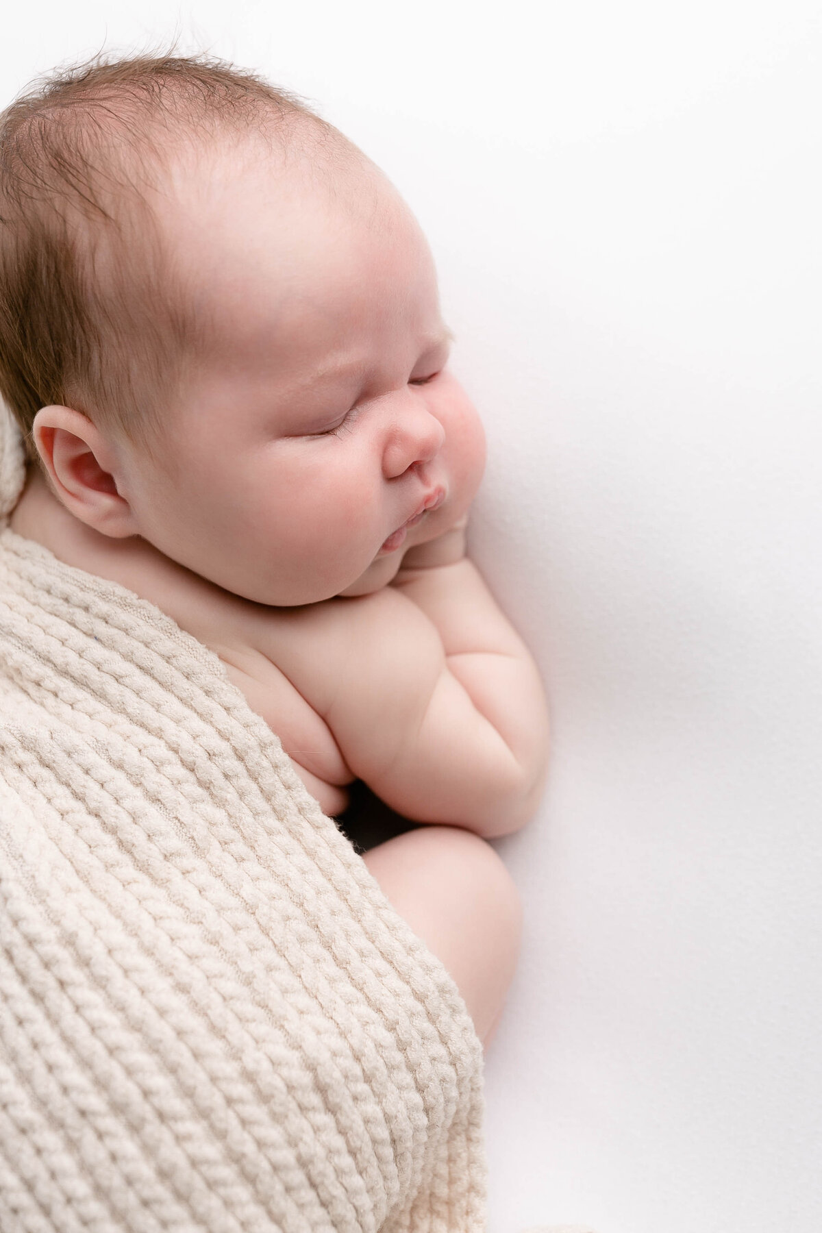 light-skinned baby sleeping on stomach  and half covered with a cream textured blanket. Image taken during portland Oregon newborn photo session.