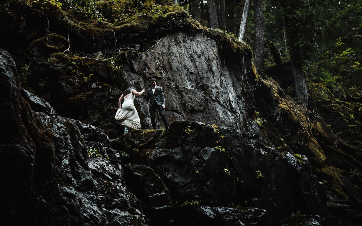 after learning how to elope in Washington State, a couple in wedding attire climbs mossy basalt cliffs