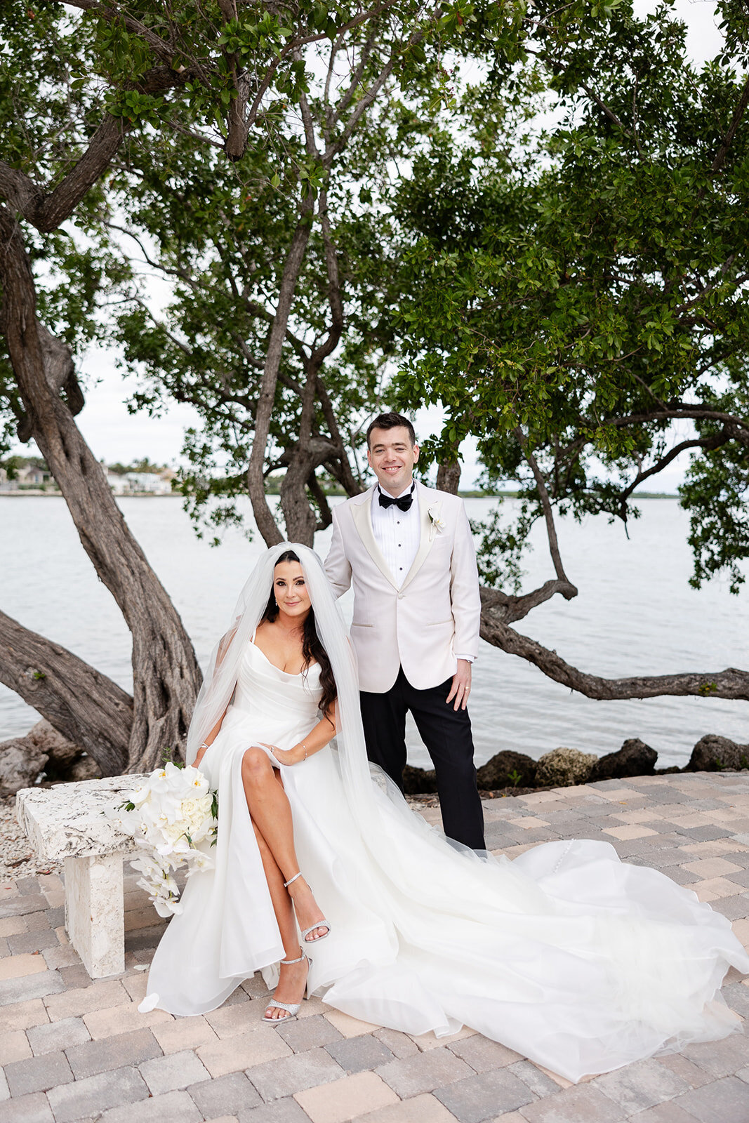 The bride and groom pose together under lush greenery, showcasing their love and elegance at Ocean Reef, Key Largo.