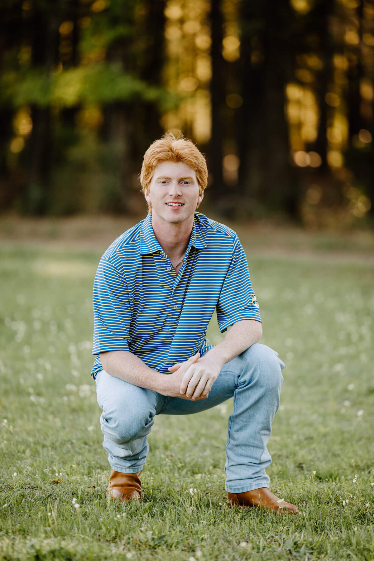 senior portrait of young man in striped shirt, jeans, and boots kneeling down in East Tx pasture