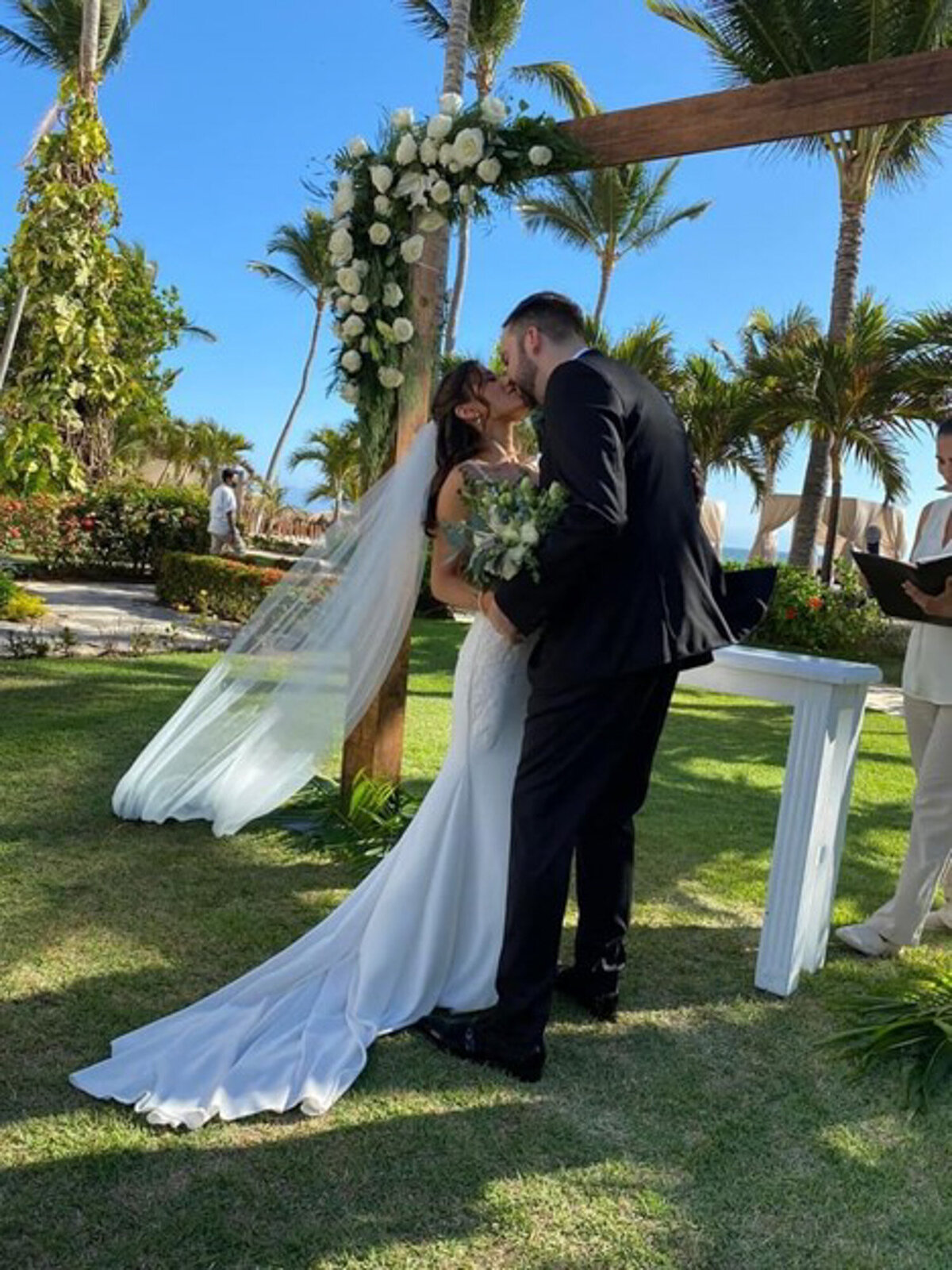 Bride and groom kissing each other while holding floral bouquet during wedding ceremony