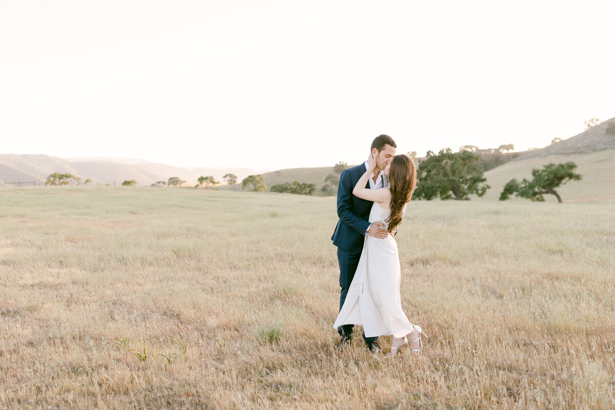 Engaged couple kiss in rolling hills of California's central coast during engagement photography session