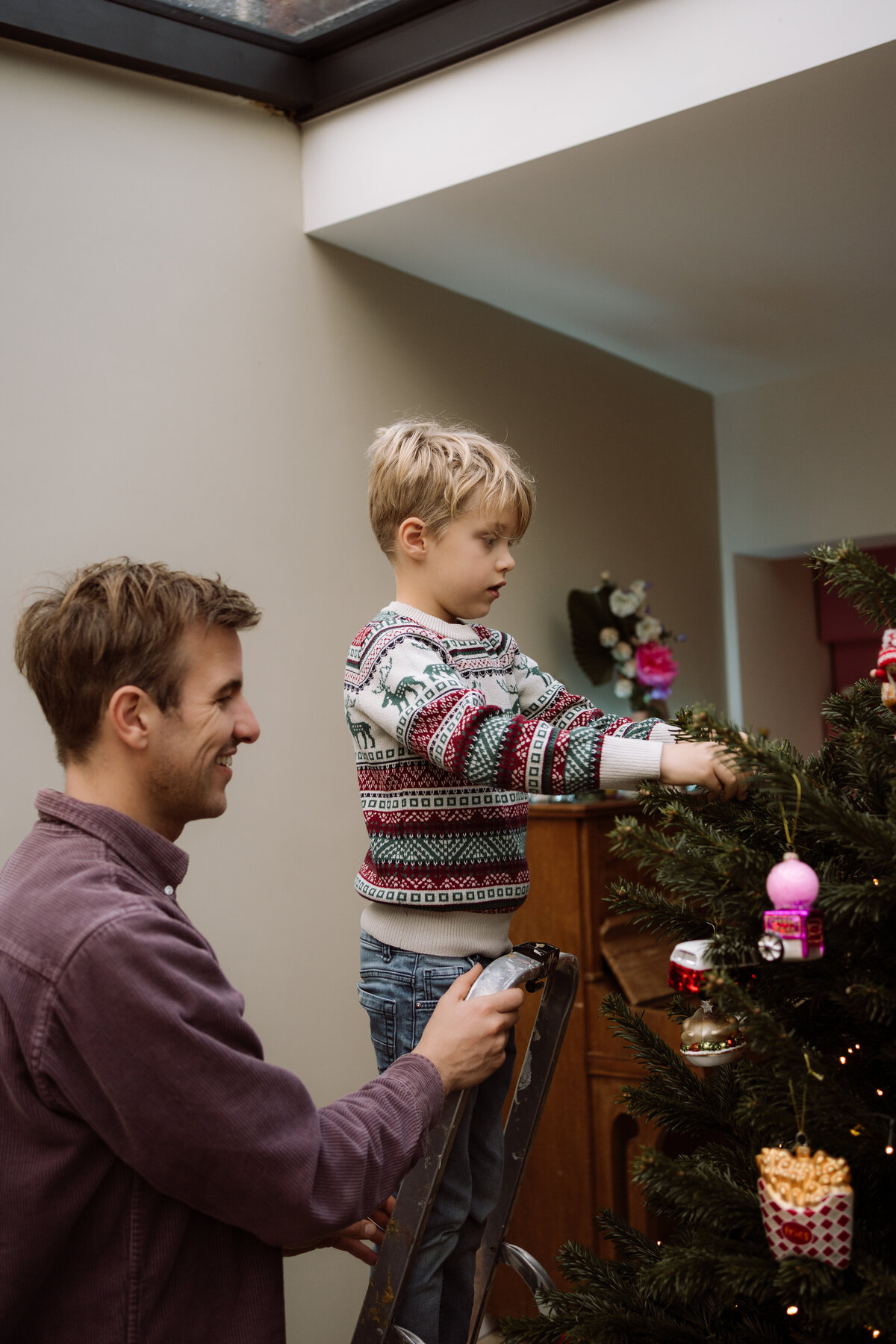 Lifestyle fotoshoot van een gezin dat samen de kerstboom optuigt, met focus op de gezelligheid en de kleine, magische momenten van de feestdagen.