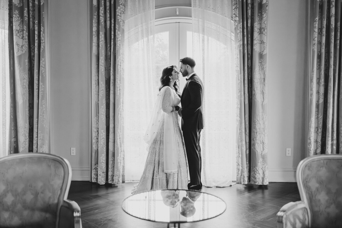 Black & White of an Indian wedding couple look at each other in front of a window indoors at the park chateau in nj