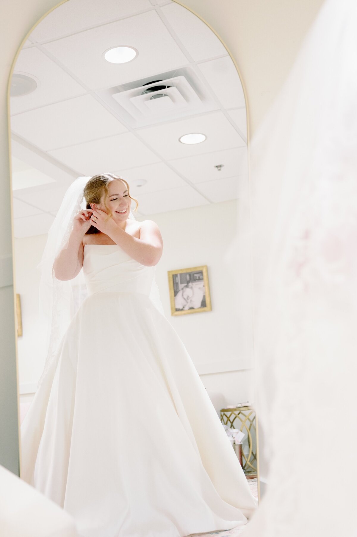 a woman in a wedding dress putting on earrings
