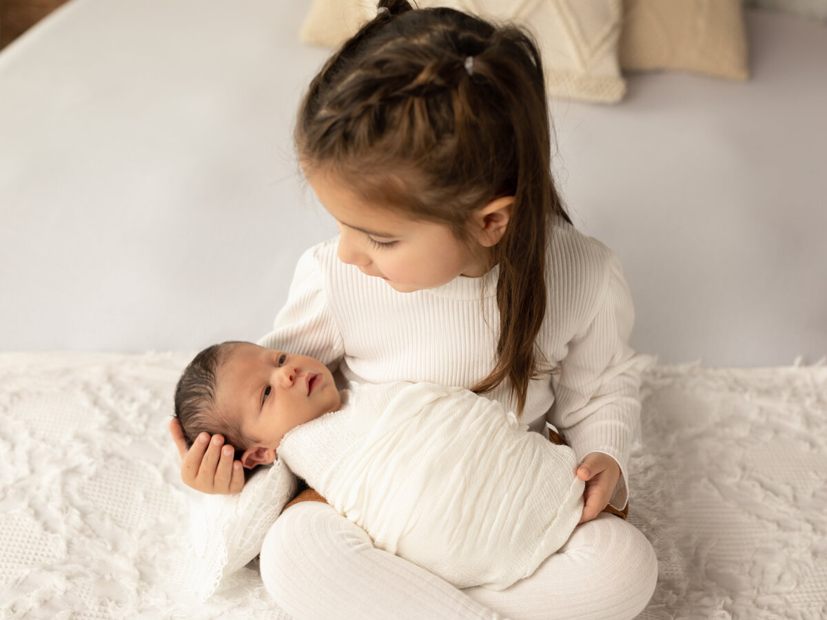big sister holding newborn brother for photoshoot