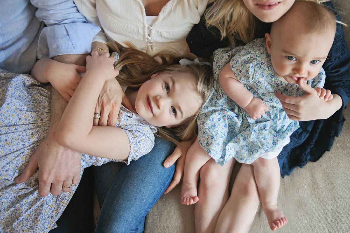 A young girl lies across her parents legs while her baby sister sits next to her