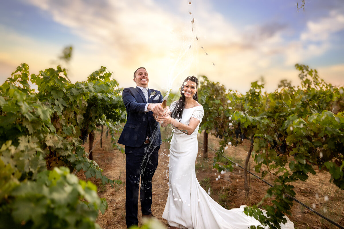 Bride and groom open a champaign bottle that sprays out, photo by sacramento wedding photographer philippe studio pro