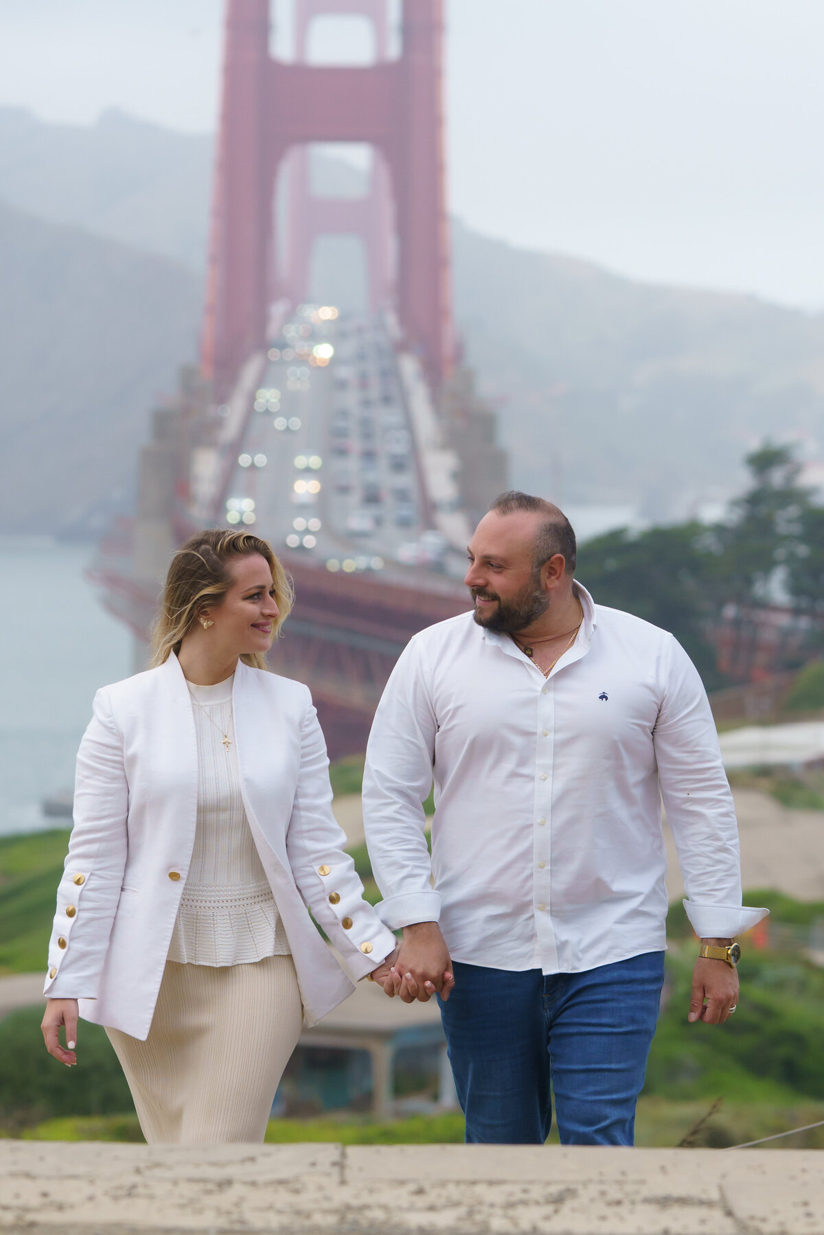 Couple holding hands and looking at each other while walking near the golden gate bridge