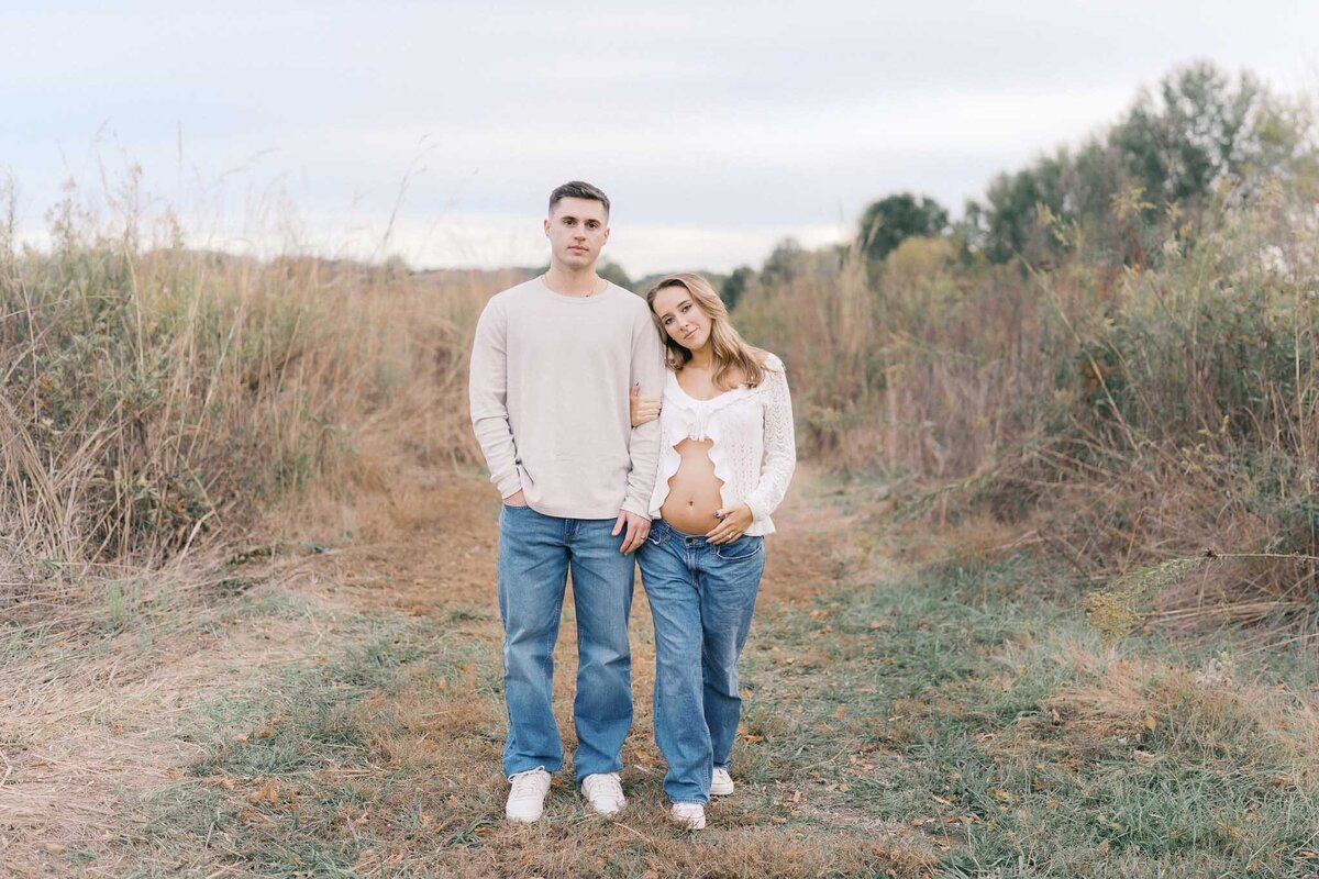 husband and pregnant wife hold hands in tall grass field in knoxville tennessee