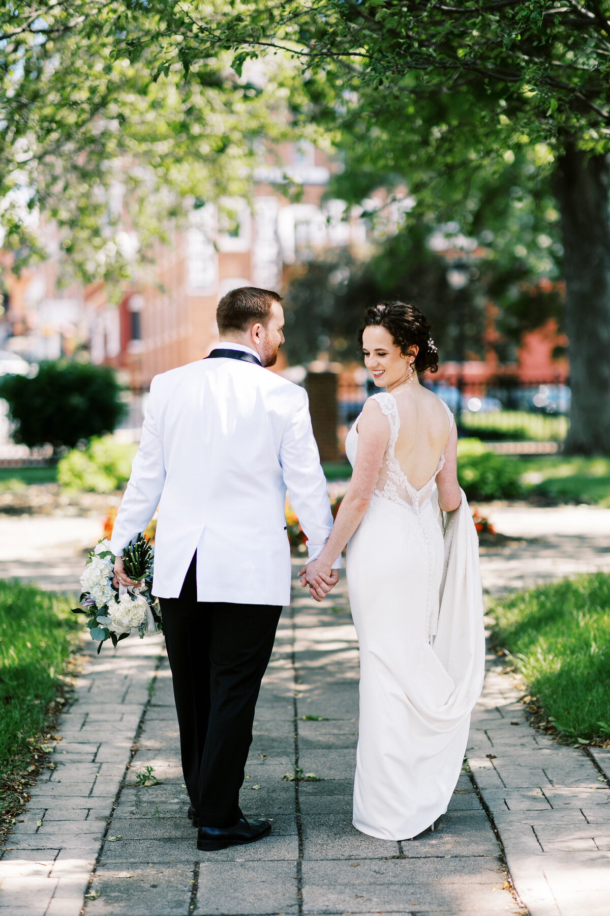 bride is looking back  while walking for her groom holding hands