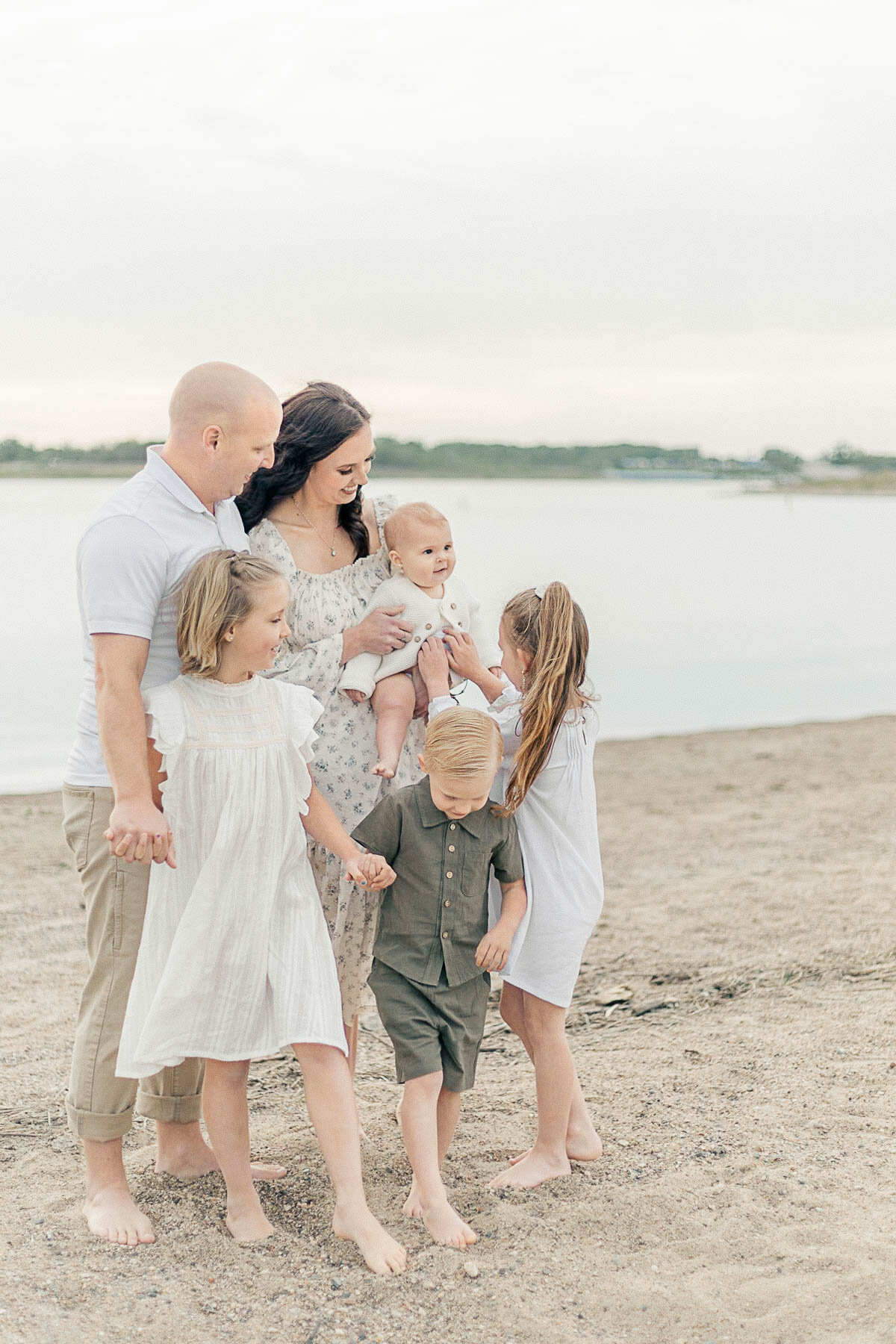 Family of six standing closely together on the sandy shoreline during a peaceful milestone session at a Kansas City beach.