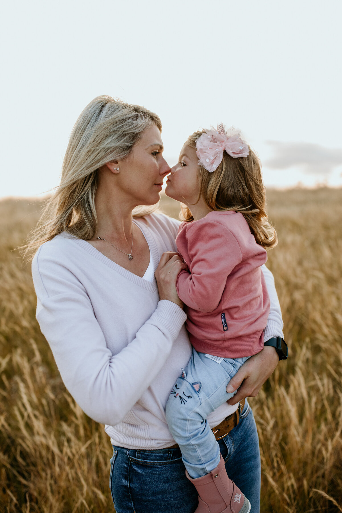 Mother and daughter nuzzle nose-to-nose, enjoying a sweet moment together in a field.