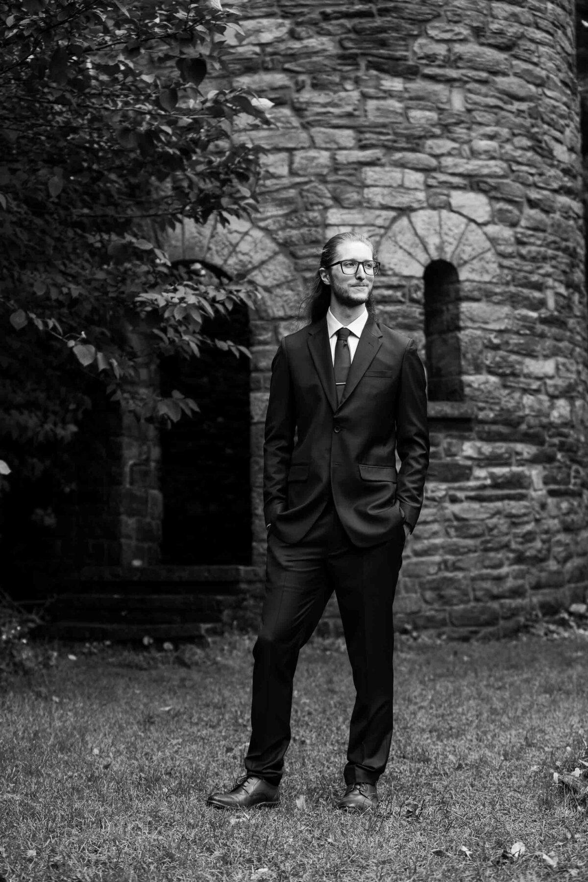 black and white image of groom standing outside of stone castle Duke Sculpture Garden at Dixon Mansion