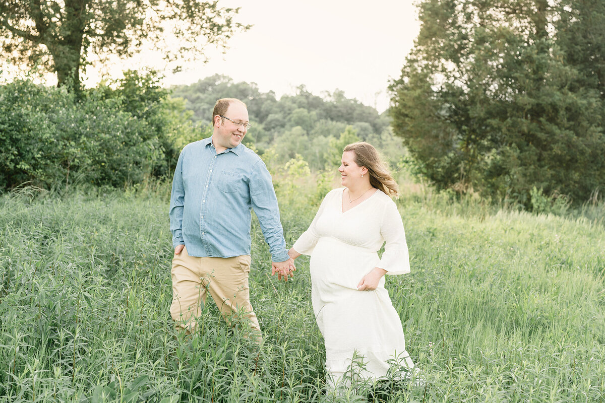 Pregnant couple walks through Louisville Ky field during outdoor maternity picture with Julie Brock Photography