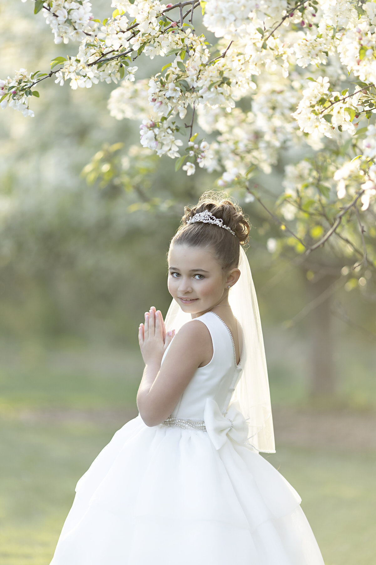 A praying young girl in a sleeveless whwite dress with a large boy under a white flowering tree