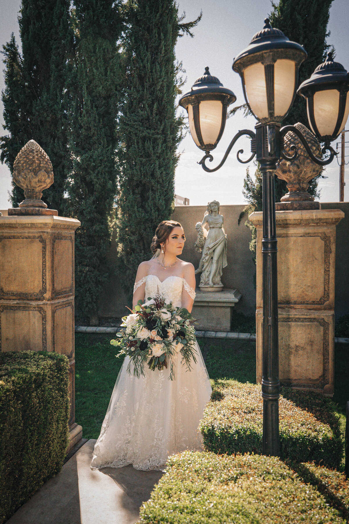 Bride holds her wedding bouquet and stands in grand garden