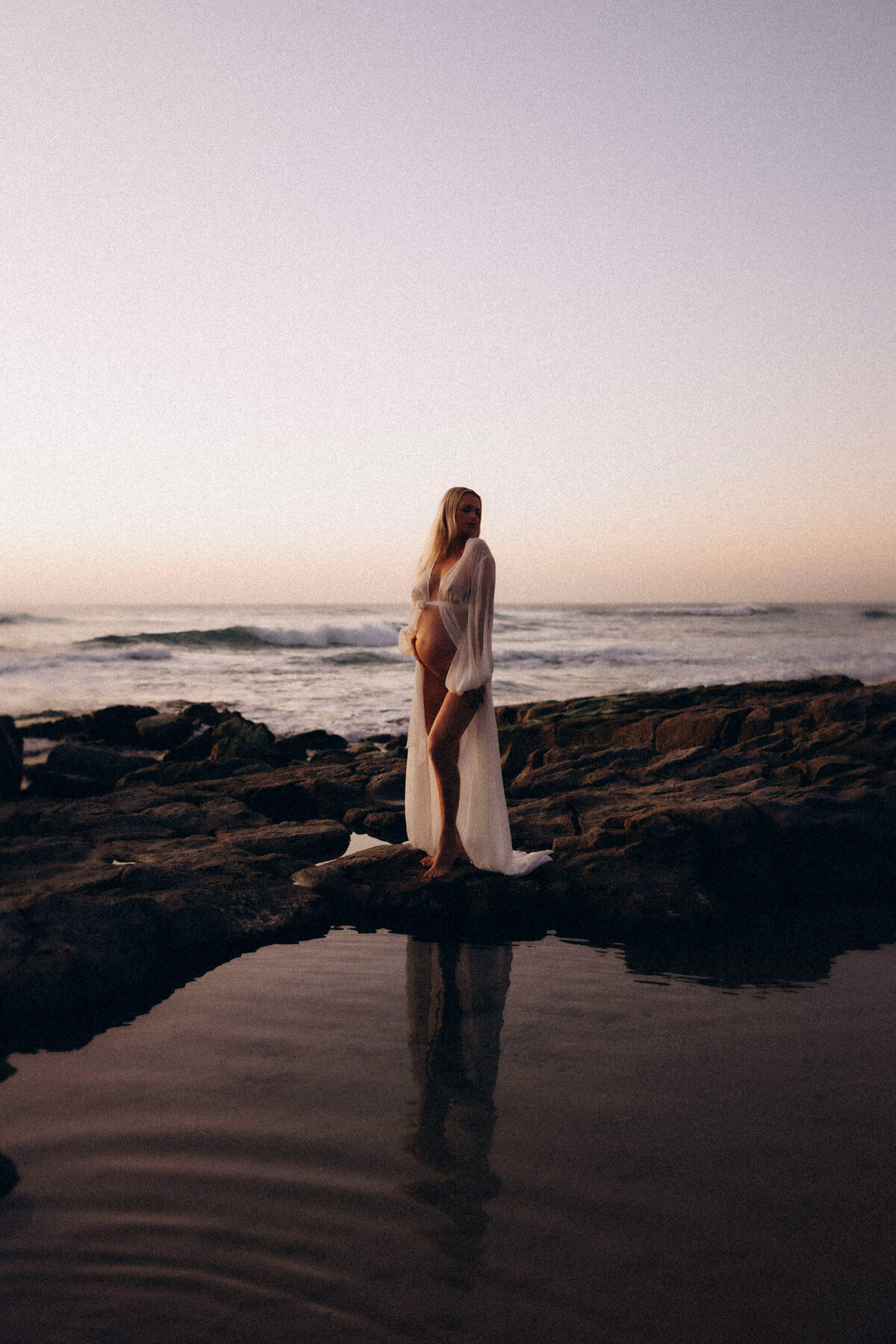 pregnant woman standing on rocks on the beach