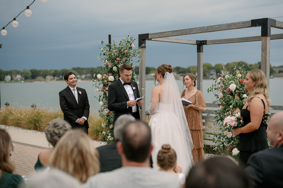 Outdoor waterfront ceremony at Boatwerks Waterfront Venue overlooking Lake Macatawa in Holland Michigan with floral arch and wedding guests.