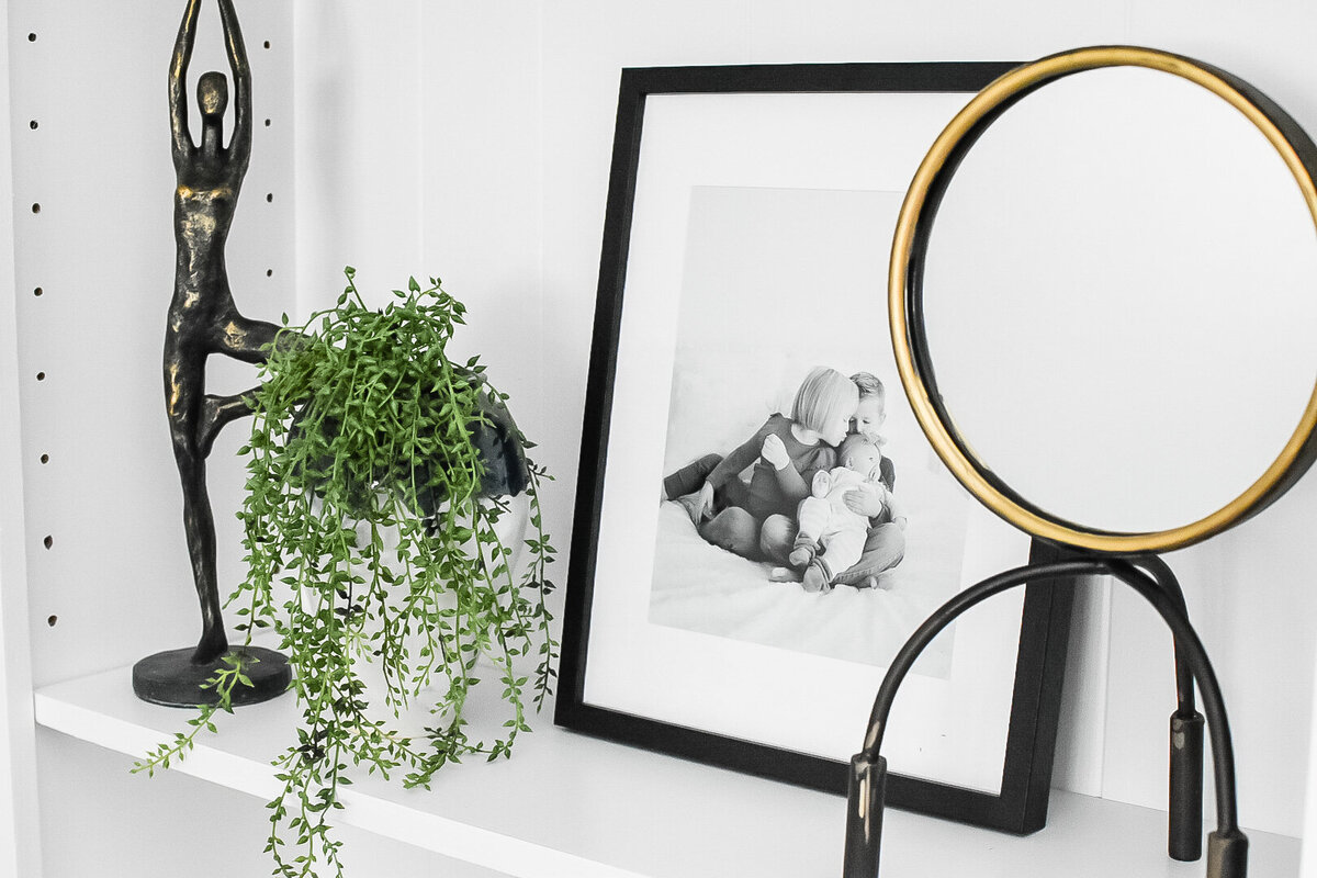 A framed black and white family photo sits on a bookshelf next to a plant and modern sculpture