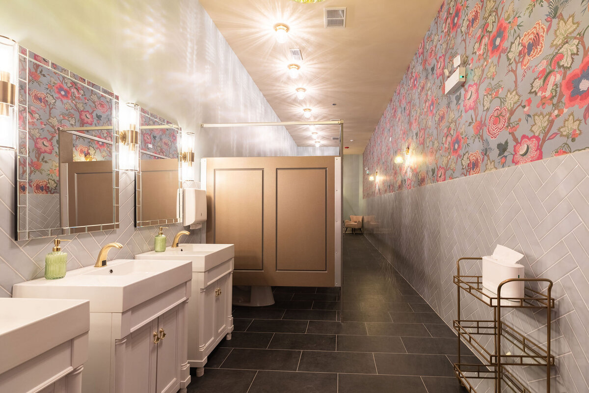 long shot of guest bathroom for women in Bloom Events space, accented with vintage green chandeliers and sconces and floral wallpaper