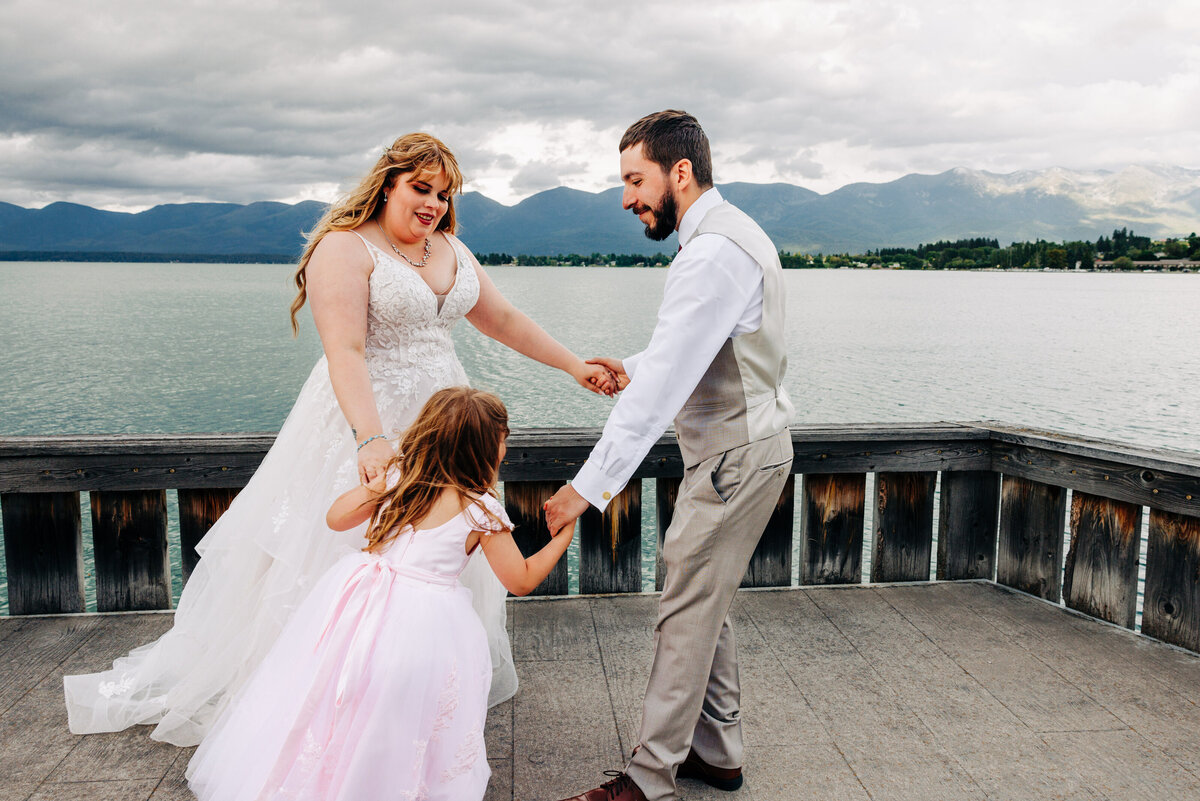 Bride, groom, and daughter dancing on dock at Kwataqnuk Resort in Polson, MT