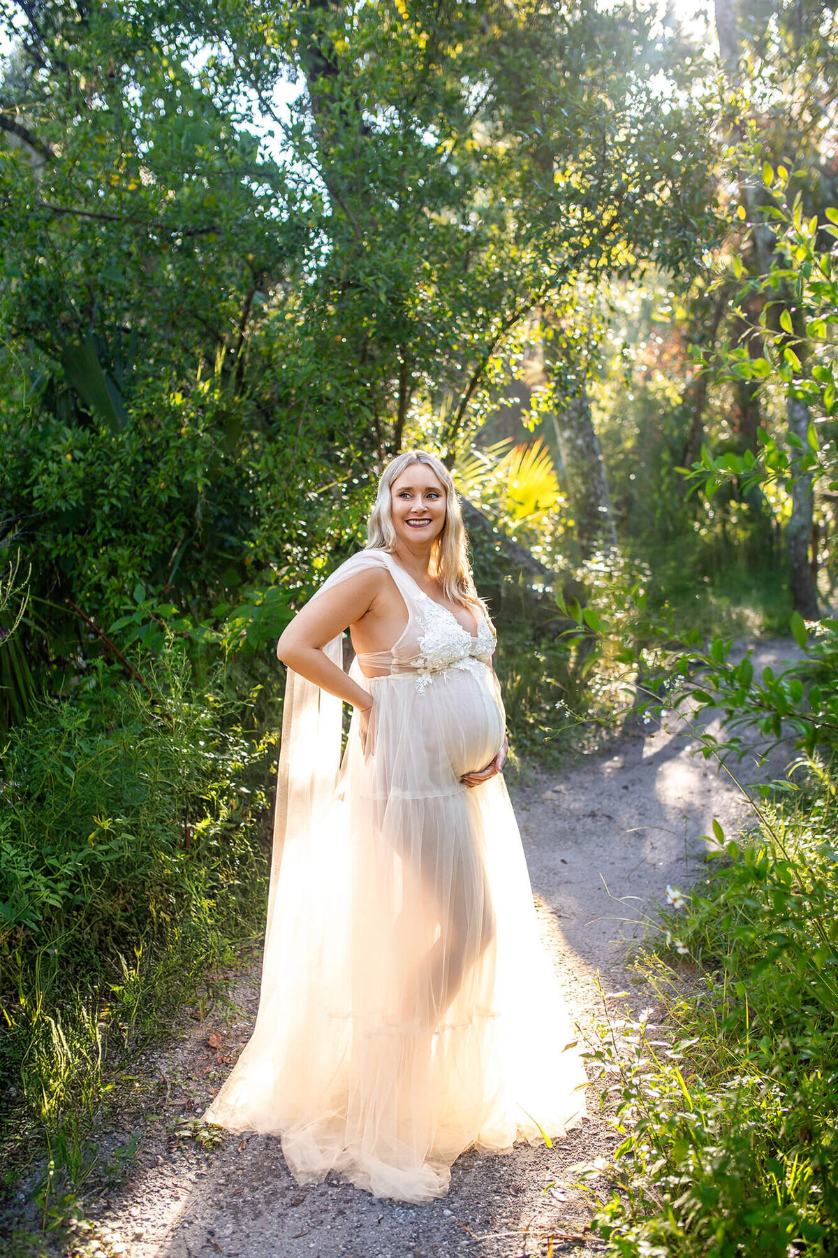 Pregnant women in long white maternity gown, glowing with light from behind at Hillsborough River State Park 