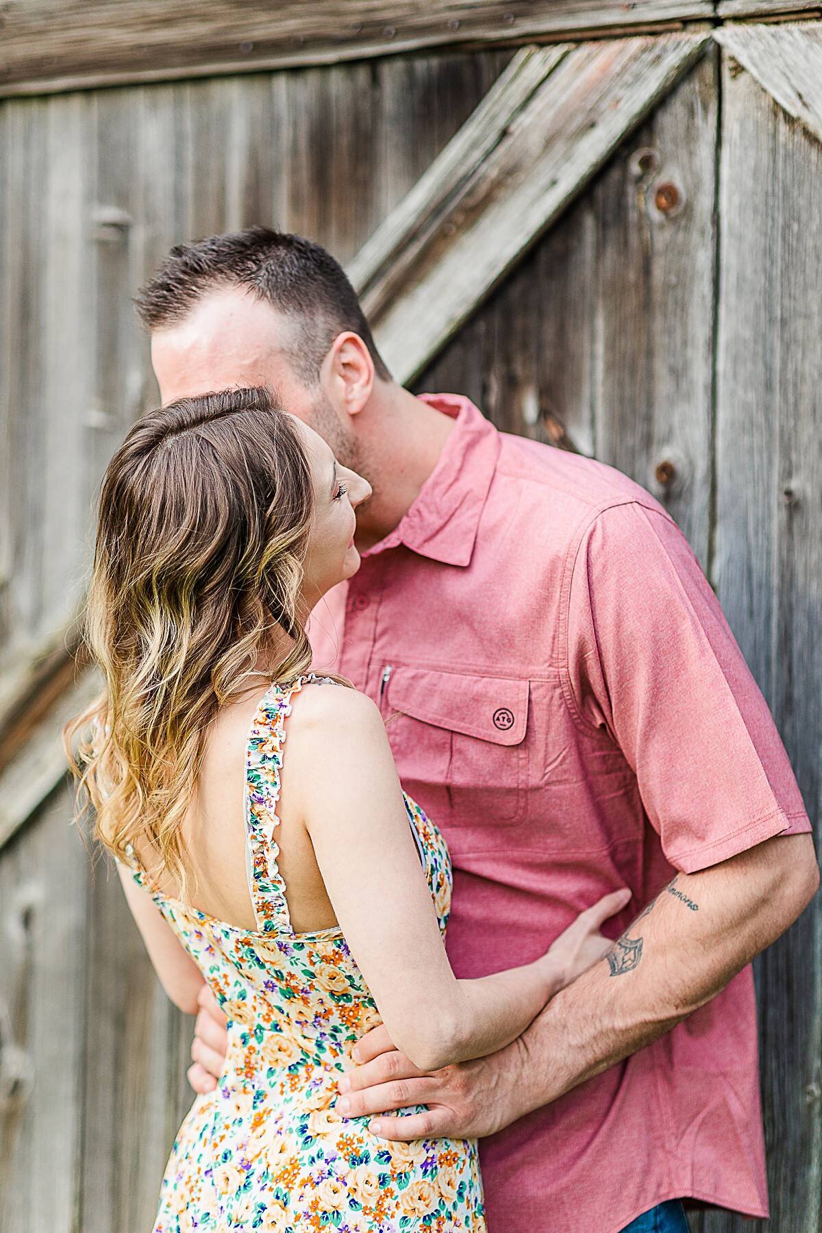 couple-kissing-while-leaning-against-old-barn