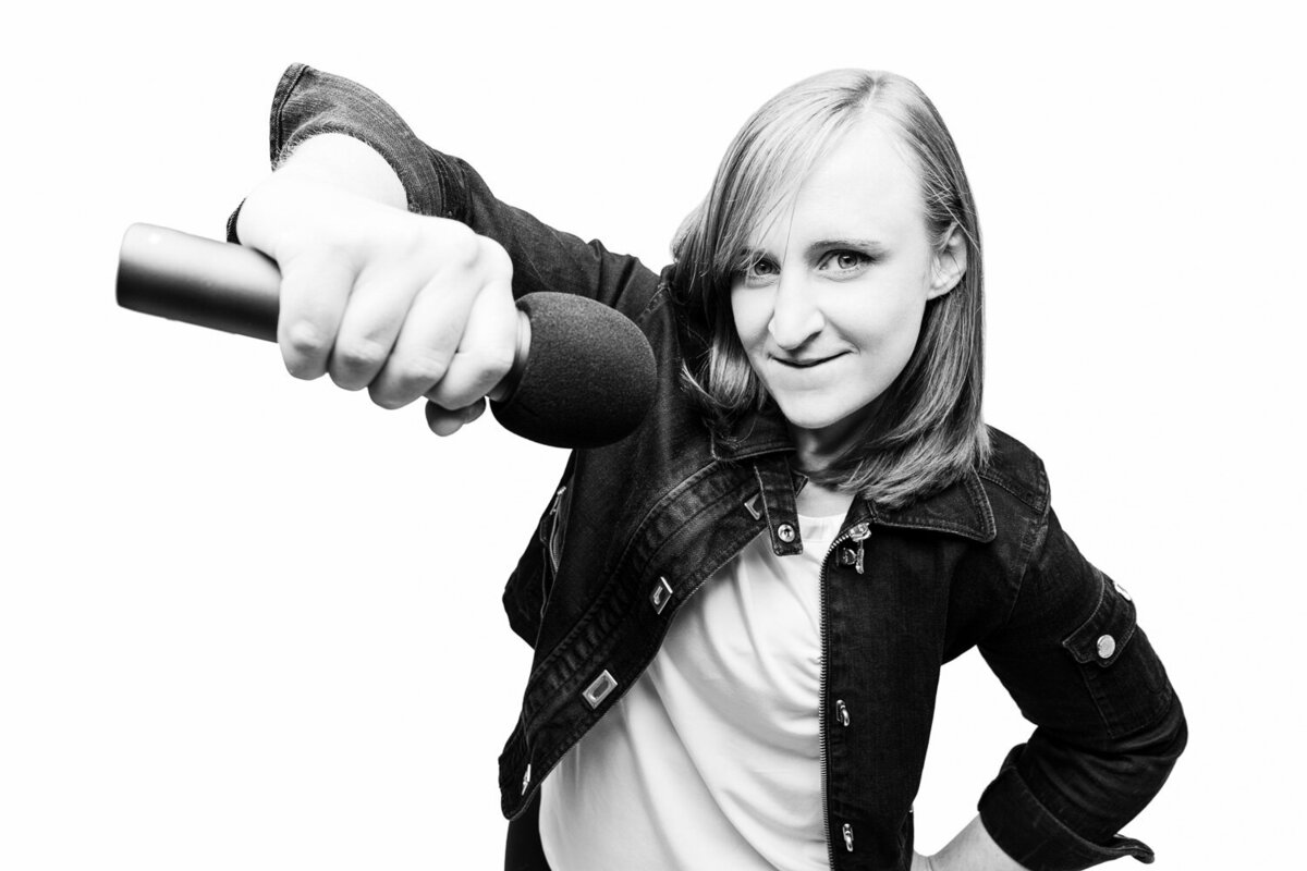 Bold editorial-style personal branding portrait of a comedian pointing a microphone toward the viewer.