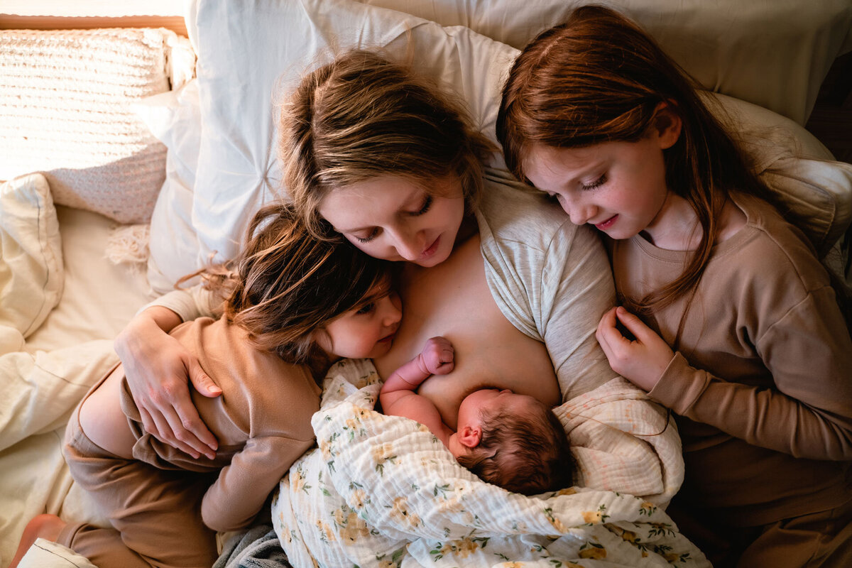 mother snuggles newborn and two daughters after home birth