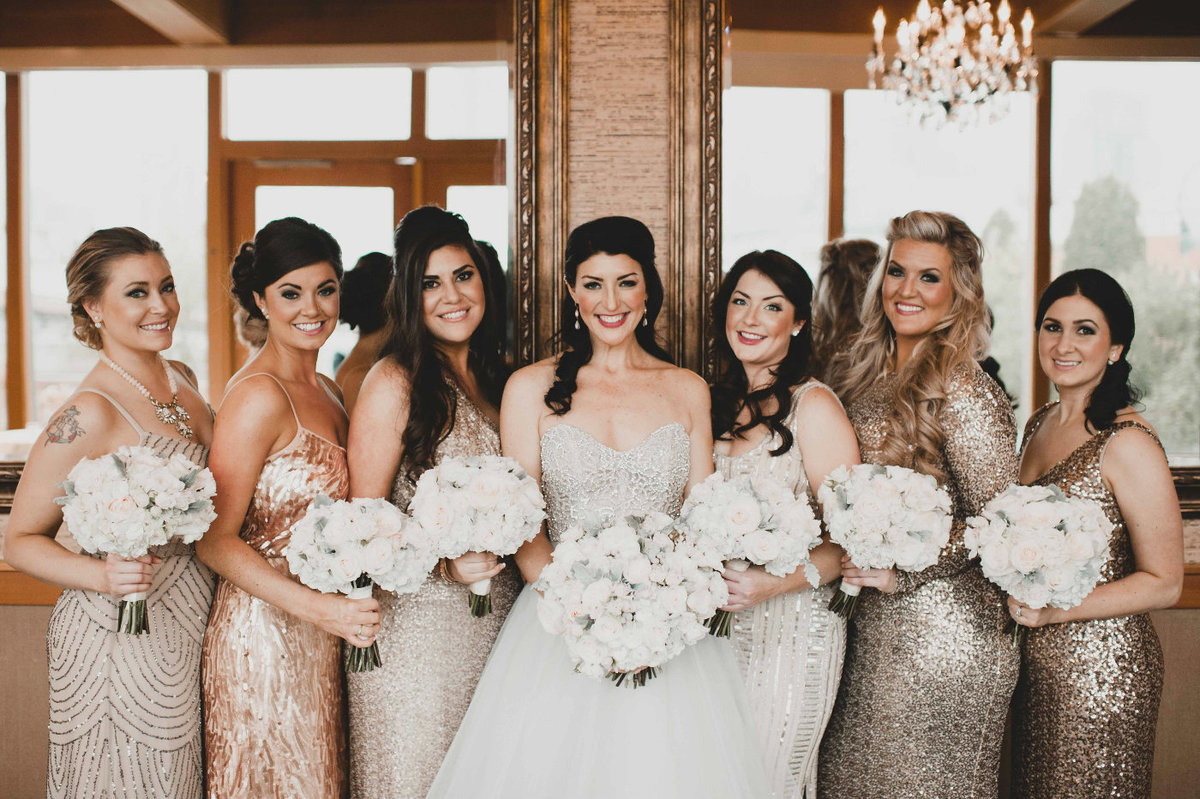 Bridesmaids wearing mixed metal sequin dresses and carrying white flowers.