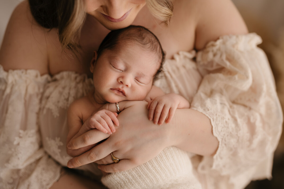 Photo of a newborn baby held in mother's arms and facing out towards the camera  during a newborn photography shoot