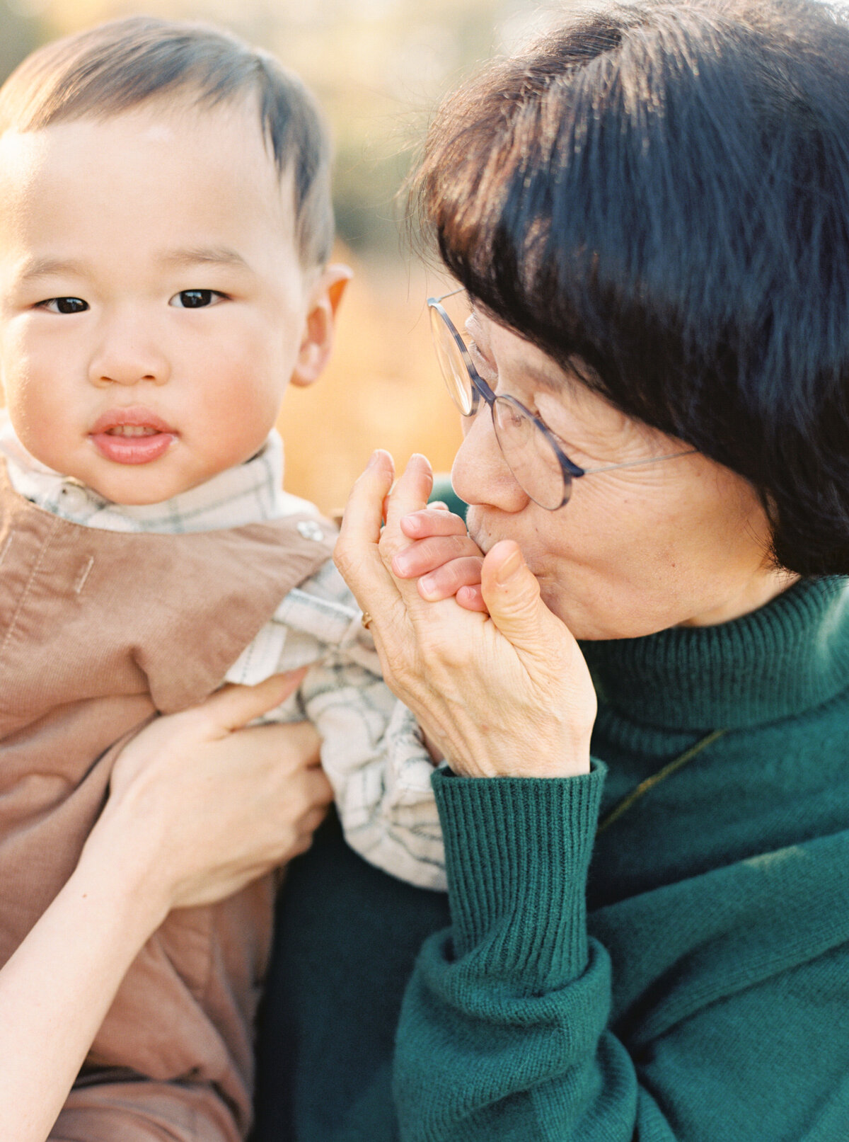 Grandma kisses hand of grandson during an extended family session in Wake Forest NC. Image by Raleigh maternity photographer A.J. Dunlap Photography.