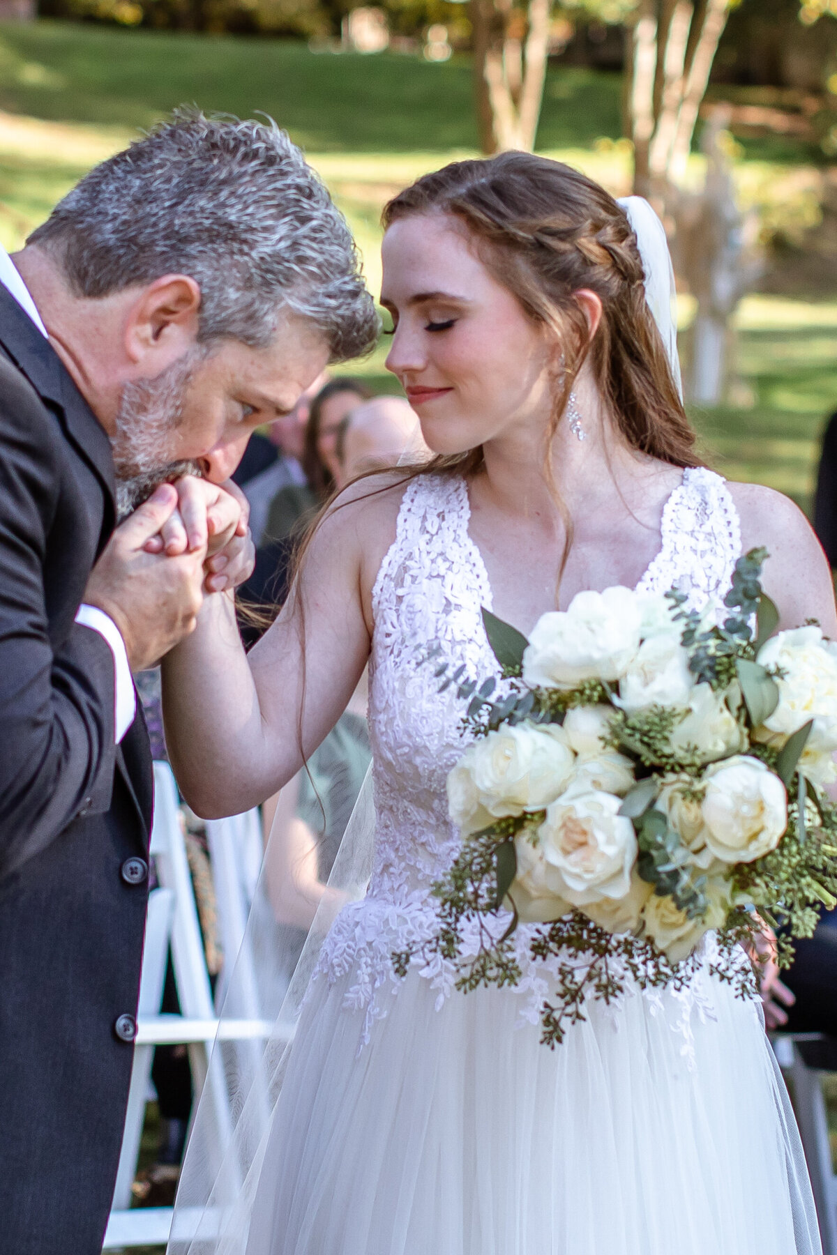 father of bride kisses her hand while she holds white bouquet at Milltown Historic District in New Braunfels Texas