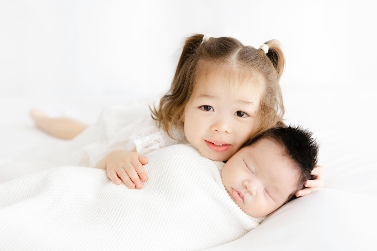 Sister snuggling baby brother for newborn photos in Alexandria VA