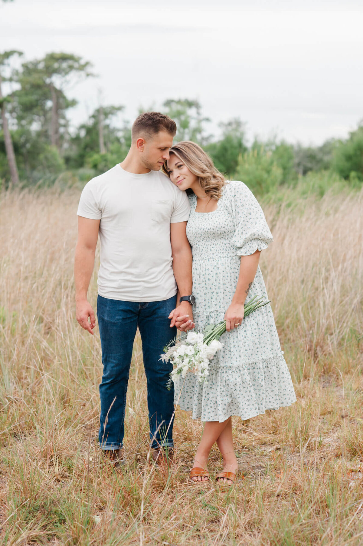 Couple standing in a tall Orlando field holding hands and husband kissing her temple