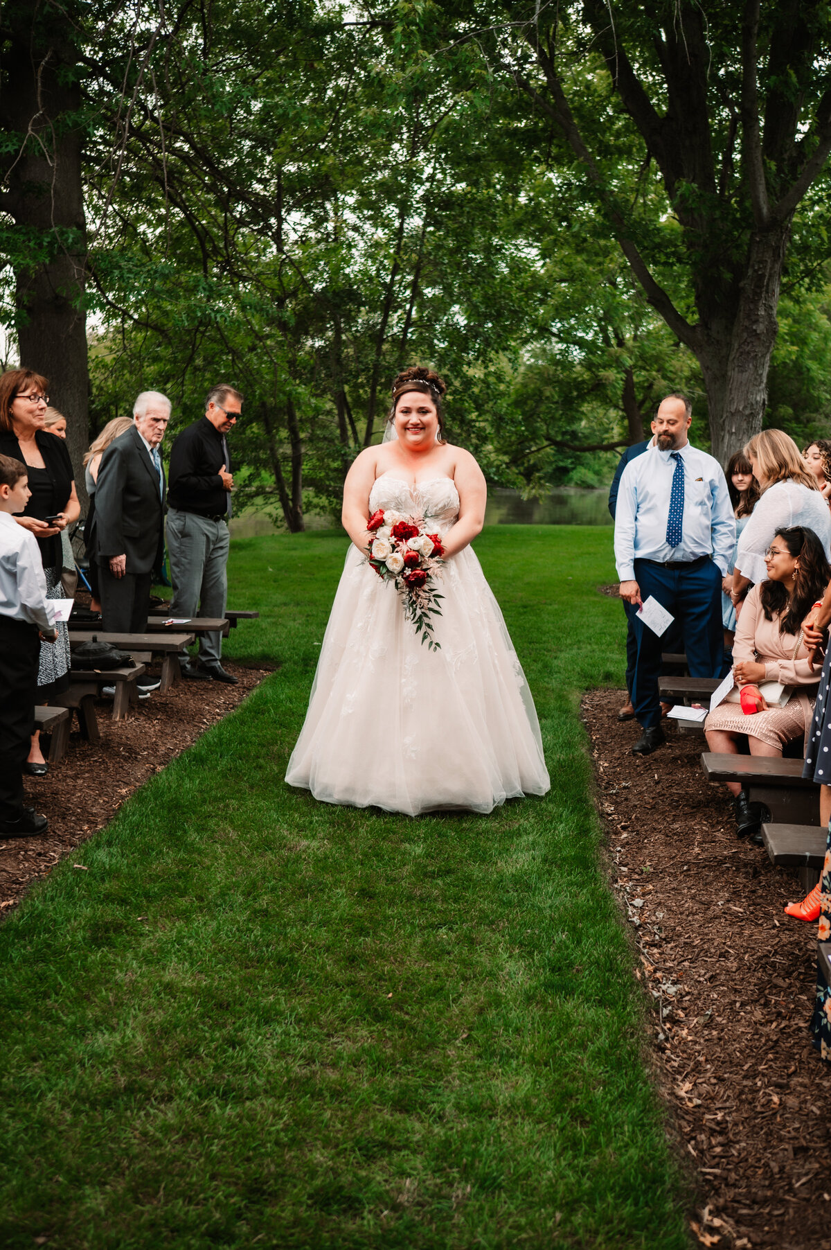 A bride holds her bouquet while walking down the outdoor ceremony aisle