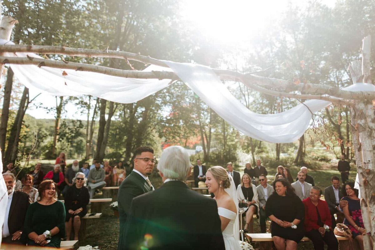 Bride and Groom standing underneath canopy surrounded by thier friends and family during their wedding ceremony in Upstate New York.